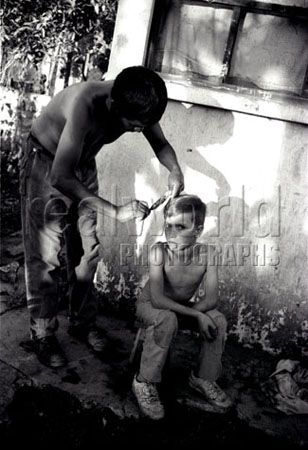 A young boy stares disgustingly at the camera after being made to have his haircut in an inpromptu barber shop on the outskirts of Guatemala City. Guatemala, Central America. 